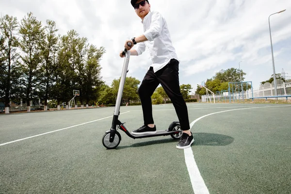 Homem moderno em roupa elegante preto e branco montando scooter elétrico na cidade — Fotografia de Stock