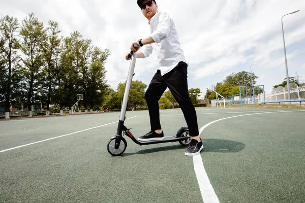 Hombre moderno en elegante traje blanco y negro montando scooter eléctrico en la ciudad — Foto de Stock