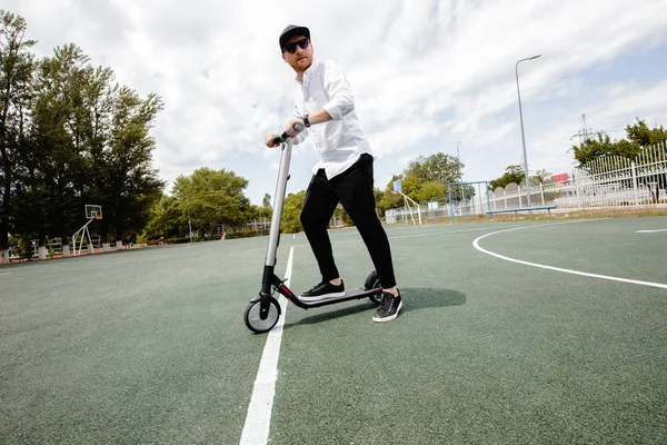 Moderne mens in stijlvolle zwart-witte outfit paardrijden elektrische scooter in de stad — Stockfoto