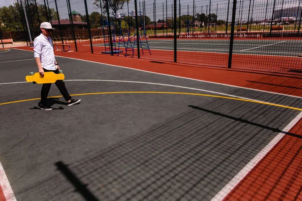 Homme moderne dans des promenades élégantes usure à l'aire de jeux de sport avec skateboard jaune à la main — Photo