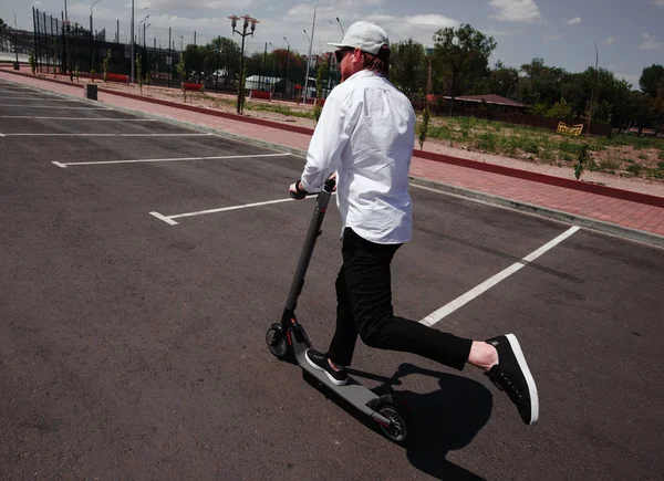 Homem moderno em roupa elegante preto e branco montando scooter elétrico na cidade — Fotografia de Stock