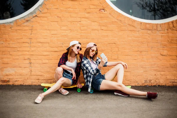 两个穿着嬉皮士服装的年轻快乐的女孩朋友坐在长板上, 在电话里自拍自拍 — 图库照片
