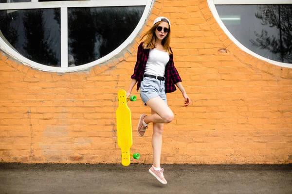 Junges fröhliches Mädchen posiert mit gelbem Skateboard gegen orangefarbene Wand — Stockfoto