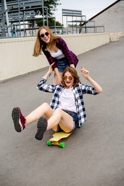 Dos amigas sonrientes divirtiéndose montando longboard amarillo en la calle. Concepto de amistad —  Fotos de Stock