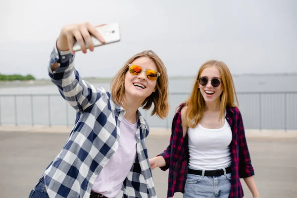 Dos jóvenes amigas felices en hipster haciendo selfie por teléfono —  Fotos de Stock