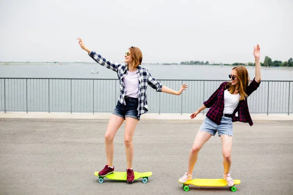 Két mosolygó nő meg tanulás lovaglás longboard, egymást segítve. Barátság koncepció — Stock Fotó