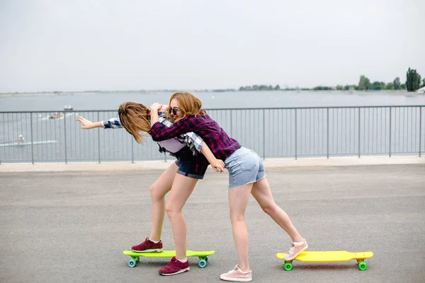 Dos amigas sonrientes aprendiendo a montar longboard ayudándose unas a otras. Concepto de amistad —  Fotos de Stock