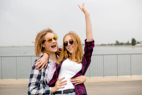 Dos amigas sonrientes abrazándose en la calle. Vacaciones, vacaciones, amor y concepto de amistad —  Fotos de Stock