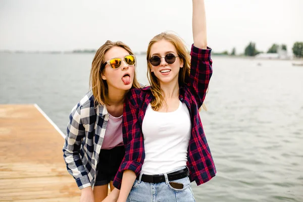 İki neşeli mutlu patenci kızlar eğleniyor ahşap bir iskele üzerinde yaz tatili hipster kıyafeti — Stok fotoğraf