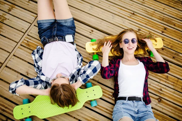 Dwa stylowe młodych dziewcząt miejskich z longboards leżą na drewnianych podłóg na ulicy. Przyjaciele zabawy i spędzić czas razem w lecie w czasie wakacji — Zdjęcie stockowe