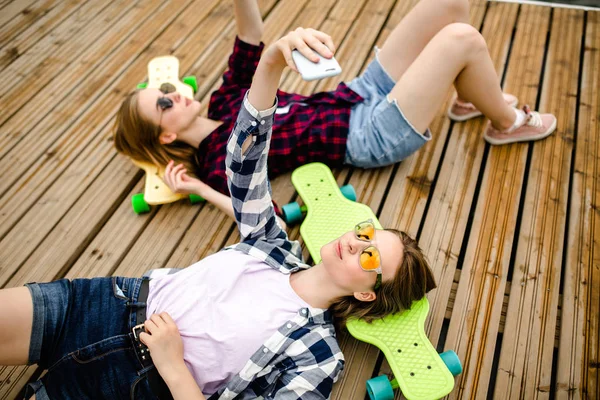 Dos chicas jóvenes en traje hipster haciendo selfie mientras están acostados en el muelle de madera —  Fotos de Stock