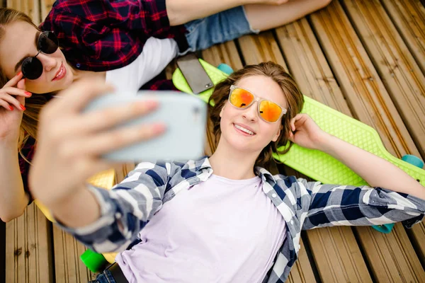 목재 부두에 함께 누워 있는 동안 selfie를 만드는 hipster 옷에 두 어린 소녀 — 스톡 사진