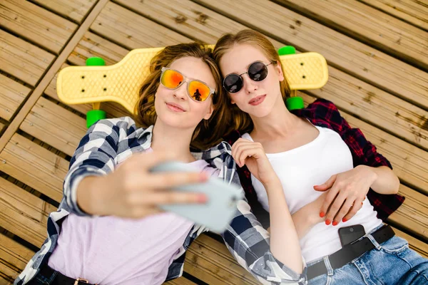 两个穿着嬉皮士服装的年轻女孩躺在木码头上做自拍 — 图库照片