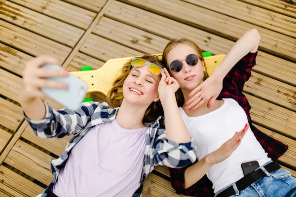 Δύο νεαρό κορίτσι σε στολή hipster κάνοντας selfie ενώ ξαπλωμένη με την ξύλινη προβλήτα — Φωτογραφία Αρχείου