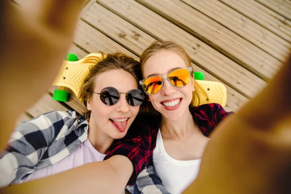 Deux jeunes filles en tenue hipster faisant selfie tout en étant couché avec sur une jetée en bois — Photo