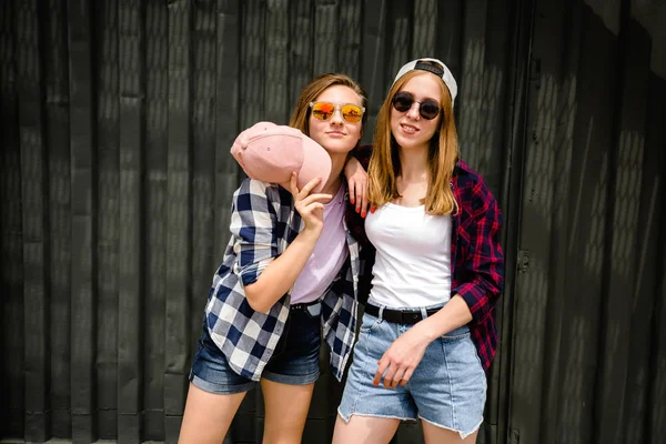 Две весёлые смешные девушки в клетчатых рубашках, позирующих на улице у стены. — стоковое фото