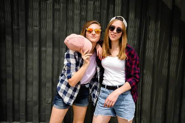 Dos alegre chica divertida con camisas a cuadros posando contra la pared de la calle en la calle — Foto de Stock