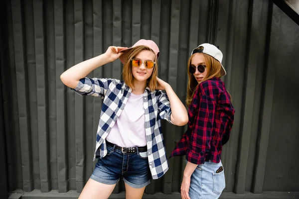 Twee vrolijke grappig meisje dragen geruite overhemden poseren tegen straat muur op de straat — Stockfoto