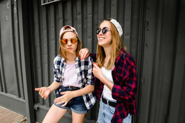 Dos alegre chica divertida con camisas a cuadros posando contra la pared de la calle en la calle —  Fotos de Stock