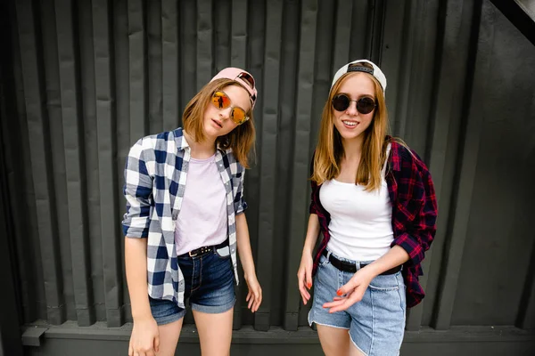 Dois alegre engraçado menina vestindo camisas xadrez posando contra parede de rua na rua — Fotografia de Stock