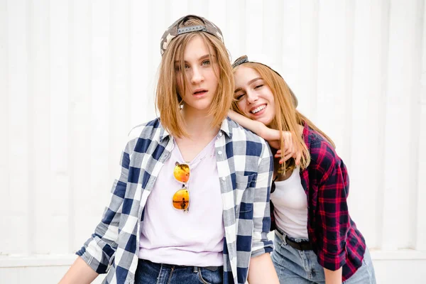 Dois alegre engraçado menina vestindo camisas xadrez posando contra parede de rua na rua — Fotografia de Stock