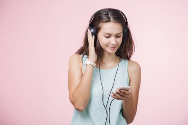 Pembe bir arka plan üzerinde müzik dinlerken kulaklık ile kahverengi saçlı neşeli kız