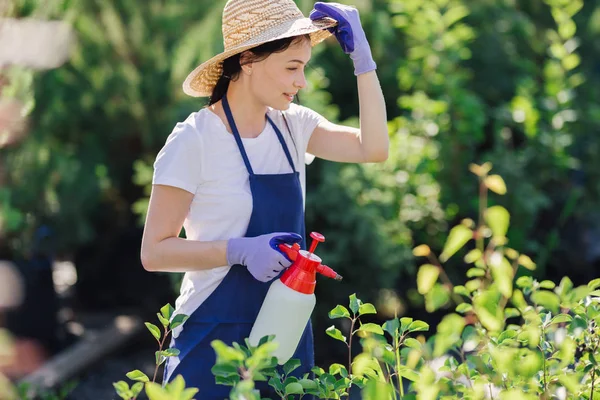 Hermosa mujer jardinero en sombrero de paja rocía las plantas de un rociador de jardín — Foto de Stock