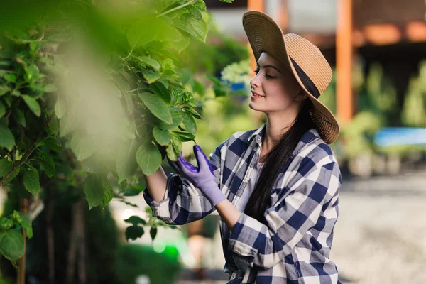 Hermosa joven con camisa a cuadros y sombrero de paja jardinería al aire libre en el día de verano — Foto de Stock