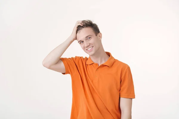 Дружелюбный европейский парень в оранжевой рубашке улыбается стоя на белом фоне — стоковое фото