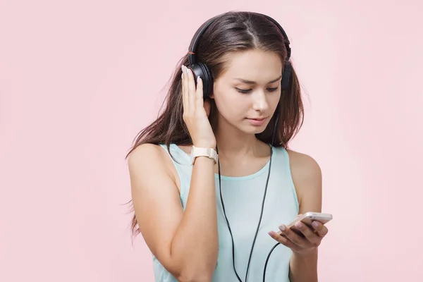 Brunhårig glad flicka med hörlurar Lyssna på musik på rosa bakgrund — Stockfoto