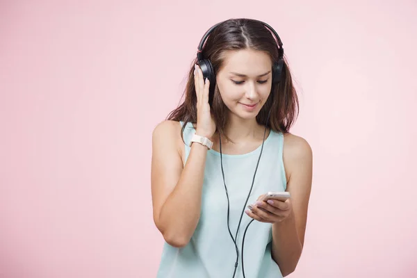 Brunhårig glad flicka med hörlurar Lyssna på musik på rosa bakgrund — Stockfoto