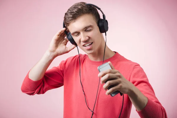 Porträtt av en ung stilig man med hörlurar leende och en musik med en smartphone — Stockfoto