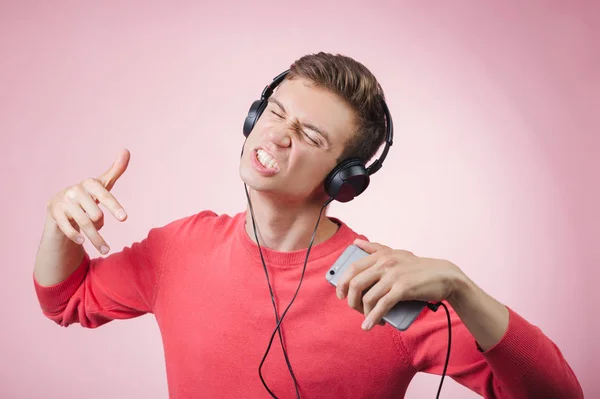 Porträtt av en ung stilig man med hörlurar leende och en musik med en smartphone — Stockfoto