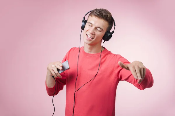 Porträtt av en ung stilig man med hörlurar leende och en musik med en smartphone — Stockfoto