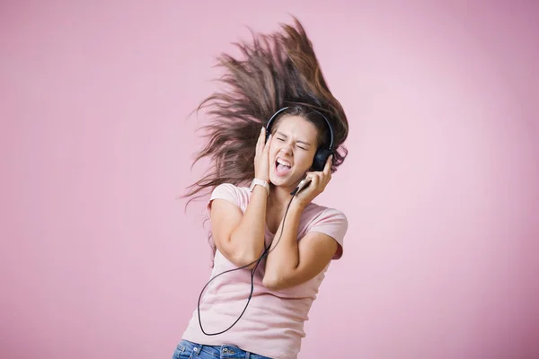 Brunhårig tjej med hörlurar Lyssna på musik med slutna ögon på rosa bakgrund — Stockfoto