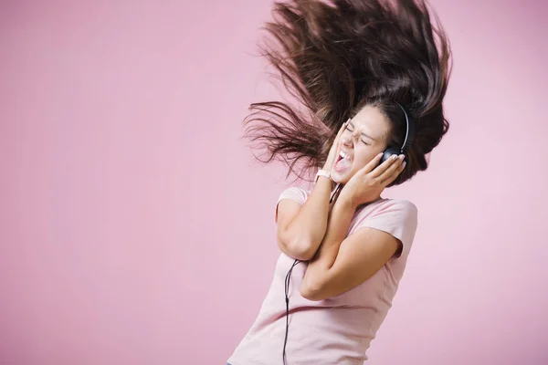 Brunhårig tjej med hörlurar Lyssna på musik med slutna ögon på rosa bakgrund — Stockfoto