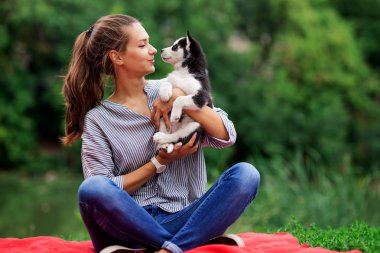 Bir at kuyruğu ve çizgili bir gömlek giymiş güzel bir gülümseyen kadın ile tatlı bir husky köpek çimlerin üstünde kırmızı paket üzerinde dinlenme süre oynuyor. Sevgi ve Evcil hayvan bakımı.