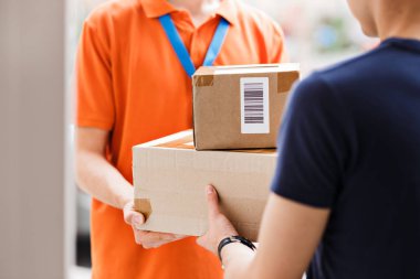 Turuncu bir T-shirt ve etiket giyen bir kişi parsel bir istemciye sağlamaktadır. Dost işçi, yüksek kaliteli gönderi hizmeti
