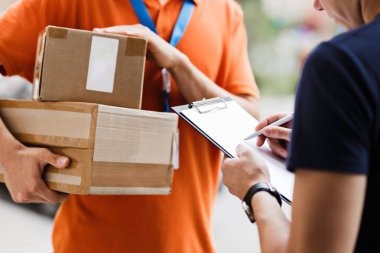 Turuncu bir T-shirt ve etiket giyen bir kişi onun imzası alış irsaliyesinde koyarak bir istemciye bir parsel sağlamaktadır. Dost işçi, yüksek kaliteli gönderi hizmeti