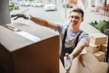 Genç bir üniforma yakışıklı gülümseyen hareket ettirmek için kutu kutu dolu minibüs boşaltma sırasında ulaşıyor. Ev taşımak, taşıyıcı Servisi