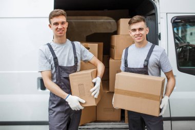İki genç yakışıklı gülümseyen işçiler üniforma giyen van kutu tam yanında duruyor. Ev taşımak, taşıyıcı Servisi