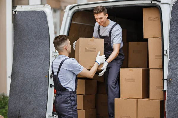 Dwóch młodych przystojny przeprowadzki noszenie mundurów są rozładunku van pełne pudła. Dom przesunąć, mover service — Zdjęcie stockowe