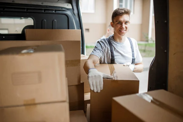 A young handsome smiling worker wearing uniform is standing next to the van full of boxes. House move, mover service — Stock Photo, Image