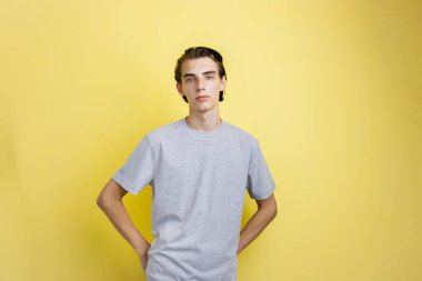 Sakin genç ince esmer yakışıklı olan mavi gözlü sarı arka plan gri t-shirt ayakta giyiyor