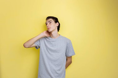 Dalgın genç ince esmer yakışıklı olan mavi gözlü sarı arka plan gri t-shirt ayakta giyiyor