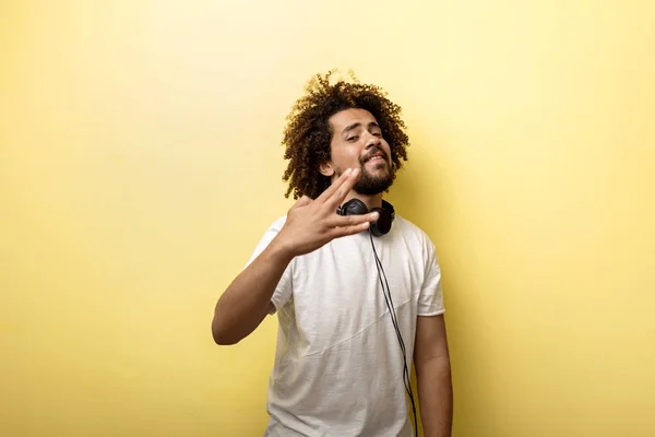 Un hombre con el pelo en un encrespamiento y auriculares en el cuello está de pie con la mano frente a él y haciendo un gesto de "Saludo Vulcano" sobre el fondo amarillo — Foto de Stock