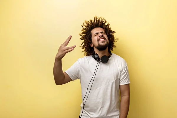En man med håret i en friss och hörlurar på halsen lyckligt leende med handen framför honom och gör en ”Vulcan Salute” gest över gul bakgrund — Stockfoto