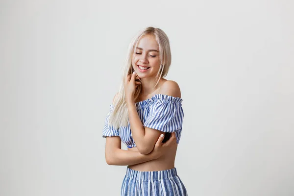 Vrolijke vriendelijke mooie blonde meisje in zomer outfit lacht zichzelf, knuffelen op witte achtergrond. Emoties, gebaren en gezichtsuitdrukkingen — Stockfoto