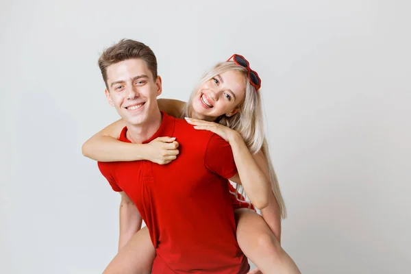 Feliz lindo alegre jovem casal em vermelho casual olhar está abraçando e sorrindo olhando para a câmera no fundo branco — Fotografia de Stock