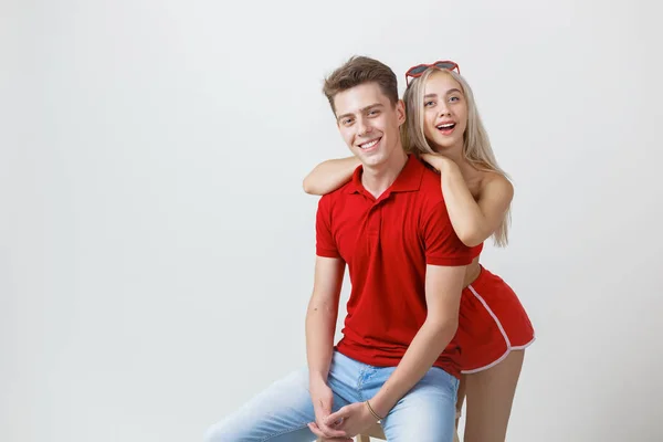 Happy lovely cheerful young couple in red casual look is hugging and smiling looking at camera on white background — Stock Photo, Image